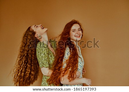 Two beautiful happy smiling women, friends, sisters have fun. Models with long natural curly hair wearing summer dresses. Hair care, beauty, friendship conception. Copy, empty space for text