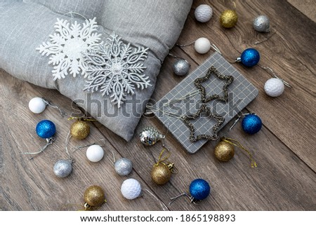 There are the gray pillow, white and silver snowflakes, diary, stars and bright Christmas balls on a wooden background