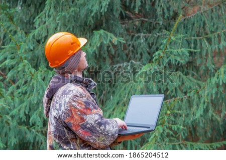 Forest engineer with a computer in his hands works in the forest. A forestry worker is engaged in forest inventory. Real people work.