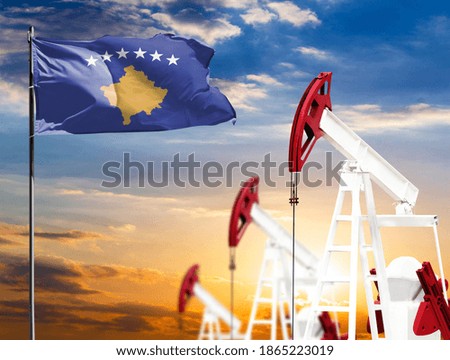 Oil rigs against the backdrop of the colorful sky and a flagpole with the flag of Kosovo. The concept of oil production, minerals, development of new deposits.