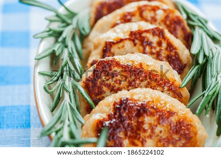 Tasty meat cutlets with rosemary in orange bowl on blue checkered tablecloth.