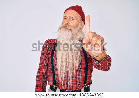 Old senior man with grey hair and long beard wearing hipster look with wool cap pointing with finger up and angry expression, showing no gesture 