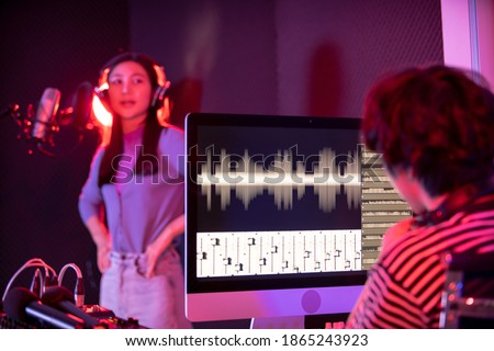 Unrecognizable Asian woman vocalist performing a singing in digital sound recording studio, Asian girl signing beautifully on the stage. Professional audio sound engineer mixing a sound in studio.