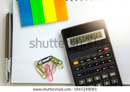Fees charged symbol. Calculator with words 'fees charged', white note, colored paper, paper clips, pen. Business and fees charged concept. Beautiful white background, copy space.