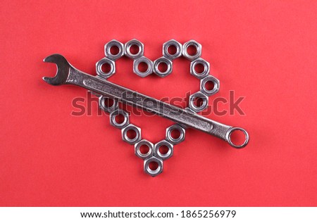 Heart made of metal nuts with a wrench on a red background. Heart symbol for valentine's day. Love, romance, creativity
