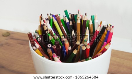 Many colored pencils lie randomly in a white pot, close up.