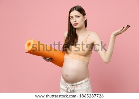 Young strong sporty fitness pregnant woman keeping hands on big belly stomach tummy with baby holding yoga mat isolated on pastel pink background studio. Maternity family pregnancy expectation concept