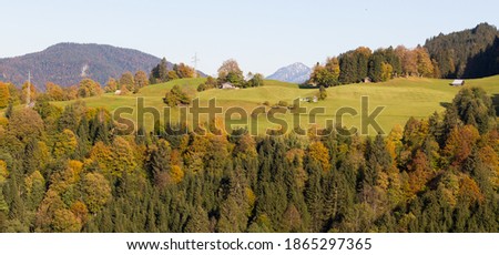 Idyllic upper bavarian mountain landscape with colorful trees and green pasture.