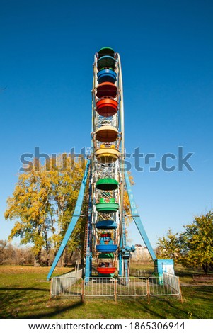An old Ferris wheel with bright booths against a blue sky. An unusual perspective