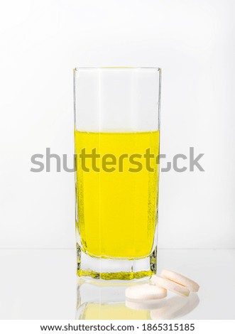 A large, white tablet with dissolves in a glass of water on a white background. Vitamin C.