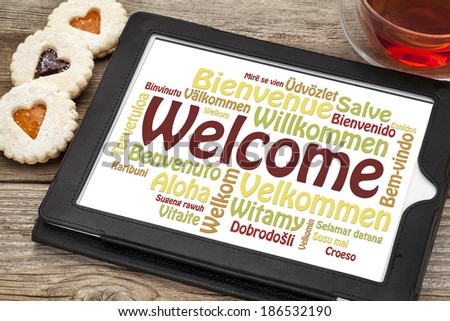 welcome word cloud in different languages on a digital tablet with a cup of tea and heart cookies