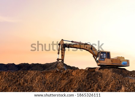 Excavator during earthmoving work at open-pit mining on sunset background. Loader machine with bucket in sand quarry. Backhoe digging the ground at construction site. Soft focus Royalty-Free Stock Photo #1865326111