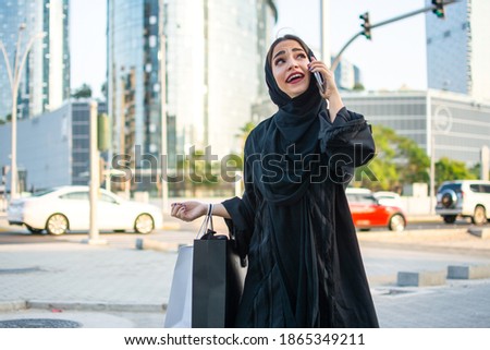 Beautiful Arabic woman carrying shopping bags and talking on mobile phone on the city street.