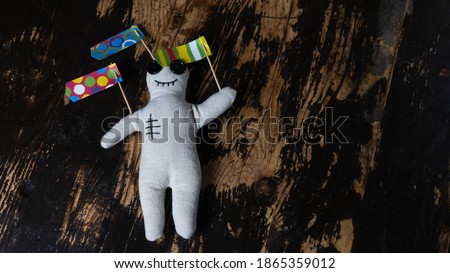 Close-up of a voodoo doll with straight pins and strange flags on dark wooden background.