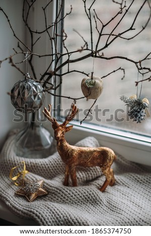 Christmas decoration - golden deer,  star and balls with dry tree branch on grey woolen scarf near window