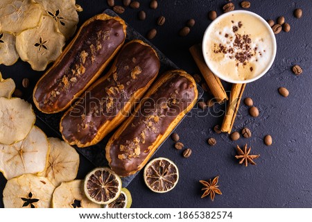 Chocolate eclair and coffee cup on dark background. Christmas composition. Royalty-Free Stock Photo #1865382574