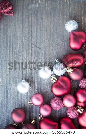 Vertical picture with small red and silver decorations for Christmas tree in bottom right corner. Copy space. New year hearts and balls on wooden grey surface. Flat layer composition for winter