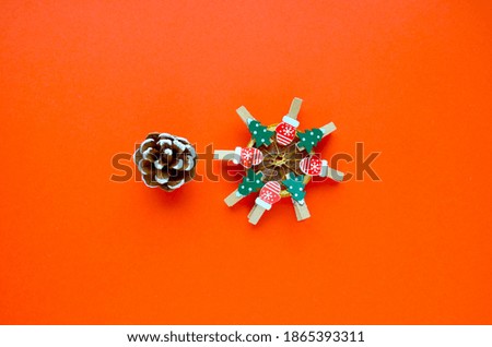 A cone and a dried lemon slice with clothespins in the form of green Christmas trees and red mittens with a snowflake pattern on a red background. The view from the top.
