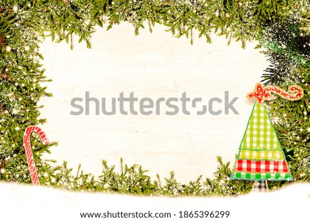 Christmas  border card. Christmas card background with a space for text on a  white wooden surface and decorated with fir branches, fabric cutout christmas tree and candy cane.