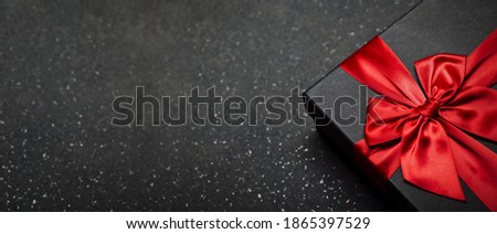 Black gift box with a red ribbon and a large bow on a granite dark background. Place for the inscription