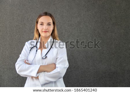 Crossing her arms confidently, female doctor posing in studio with stethoscope around her neck, standing straight and looking into camera. Copy space. Healthcare, medicine and profession concept.