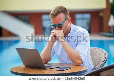 Young male businessman with laptop sitting by the pool. Open workplace. Freelancer concept. Online shopping. Vacation work