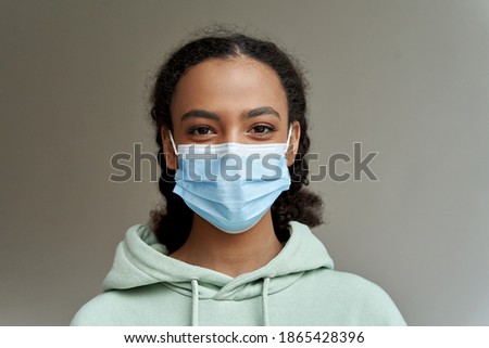 African american teen girl wearing face mask looking at camera isolated on grey background. Mixed race teenager during coronavirus. Children safety for covid protection, close up headshot portrait. Royalty-Free Stock Photo #1865428396