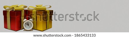 Gift red and gold boxes and white alarm clock on light background
