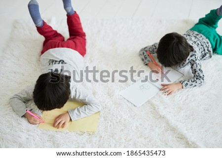 Imagination. Two concentrated little latin boys, twin brothers drawing pictures with colorful pencils in paper album while lying on the floor. Siblings involved in creative activity together