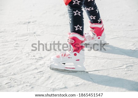 Figure skates on girl legs on the ice covered with snow and with traces made by skating. Child winter outdoors on ice rink. Ice and legs
