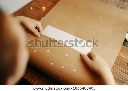 Girl's hands wrap cardboard box in kraft paper on wooden table. Concept of handmade. Packaging of gifts for holiday. Brown paper with white dots design.