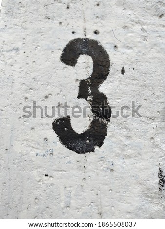 Black number three (3) on a white plastered wall background.