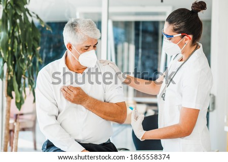 old latin man receiving vaccine shot for a mexican doctor woman with facemask for coronavirus pandemic in Mexico city