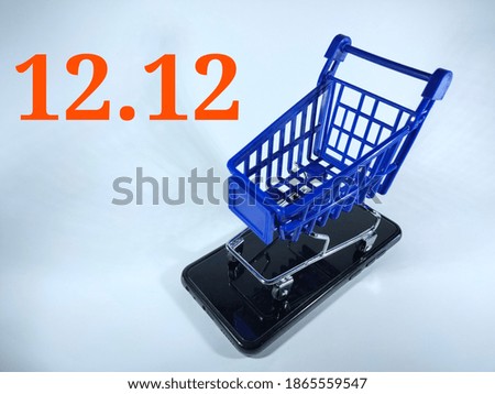 Selective focus.12.12 in orange number with blue trolly and smartphone isolated on white background.Shopping online concept.