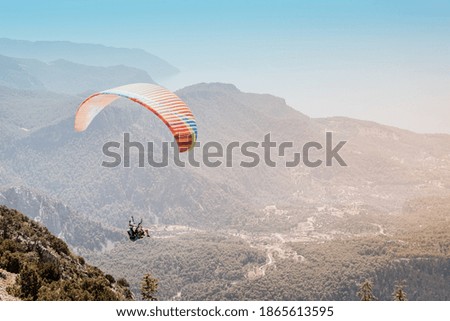 A paraglider with an instructor and a student soars against the background of wooded mountains and hills