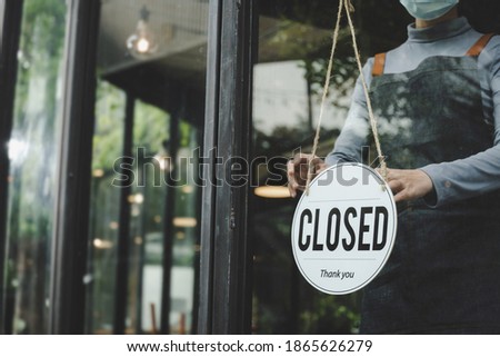 small business owner woman wearing protection face mask turning closed sign board on glass door for open cafe restaurant after coronavirus (covid-19) quarantine. reopen shop, food and drink concept