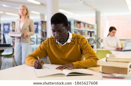 Portrait of confident african-american male student working with book in public library. High quality photo