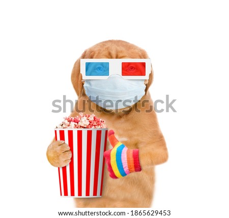 Puppy wearing 3d glasses and medical mask holds bucket of popcorn and shows thumbs up during the coronavirus epidemic. isolated on white background