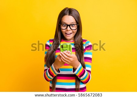 Photo of little girl hold cellphone open mouth excited wear spectacles striped shirt isolated yellow color background