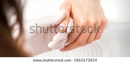 The manicurist holds the woman's thumb during a manicure procedure in the nail salon