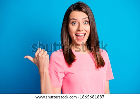 Photo portrait of amazed girl staring with opened mouth pointing blank space smiling in pink outfit isolated on vivid blue color background