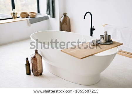 White bathtub fills with foam water in a modern apartment with stylish loft-style interior design, home decor. Spa concept, relaxation. Soft selective focus.