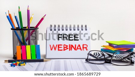 On the table are colored pencils in a stand, brightly colored stickers, glasses and a notebook with the inscription FREE WEBINAR. Motivating concept. Call to action