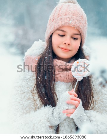 Closeup winter portrait of little girl with snowflakes on long brunette hair enjoying snow winter time on street in city. Warm white winter clothes, true emotions, christmas mood