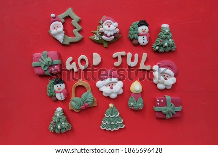 Creative swedish and norwegian Merry Christmas, God Jul, with wooden letters and marzipan Christmas symbols over red color background