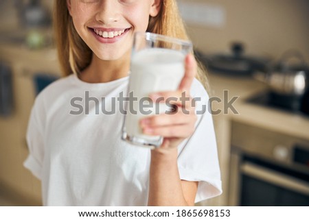 Cropped photo of a blonde kid with a happy smile holding a glass of milk