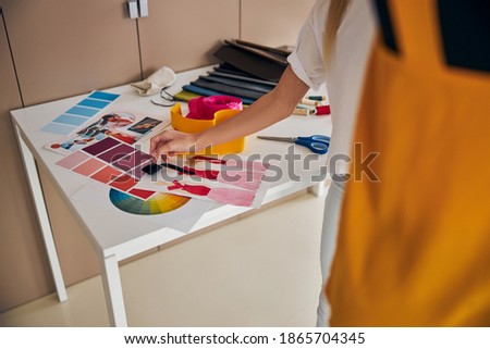 Cropped photo of a blonde Caucasian girl standing at the cutting table in her workshop