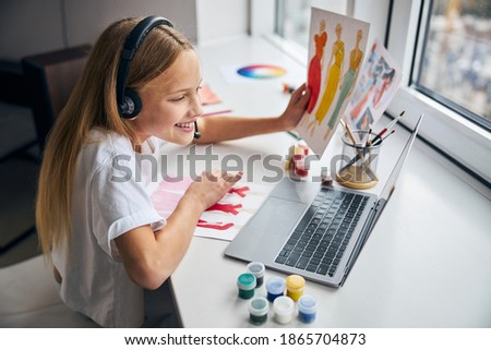Side view of a smiling girl with dress sketches in one hand staring at her laptop