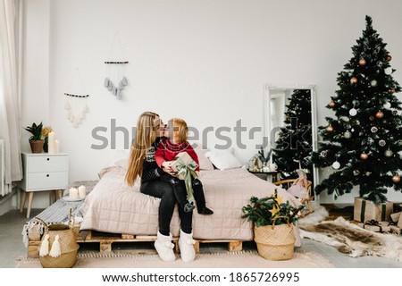 Merry Christmas and Happy Holidays. Mom gives a gift to her daughter near the Christmas tree. Cheerful mother hugging cute baby child girl together at home. Happy New Year 2021.