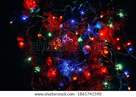 Christmas tiny lights playing in all colors on a black background. Abstract art. Christmas bulbs. The light bulbs on the wire intertwine. Red, blue, green nad more shadows of colors.